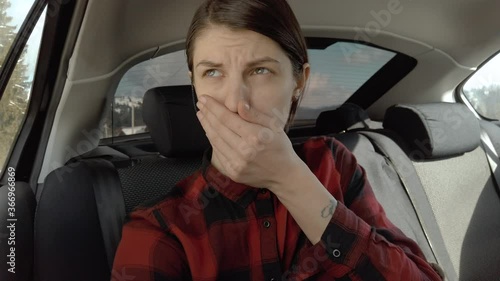 Woman sits in the back seat of a car and feels bad. Female vomiting in the back seat of a car. Covers her mouth with her hand