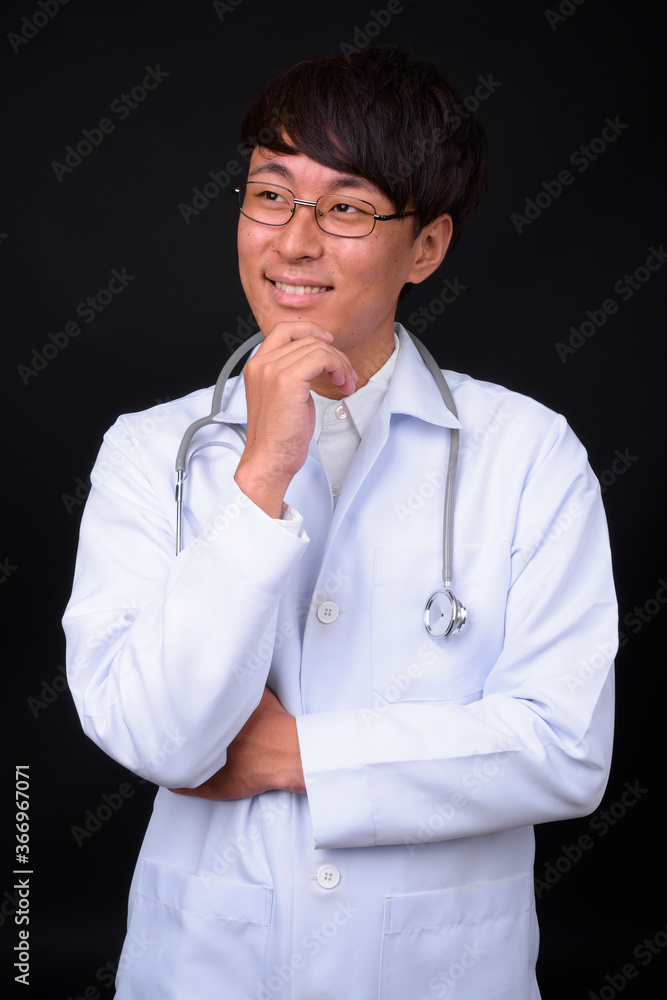 Young handsome Asian man doctor against black background Young handsome Asian man doctor against black background