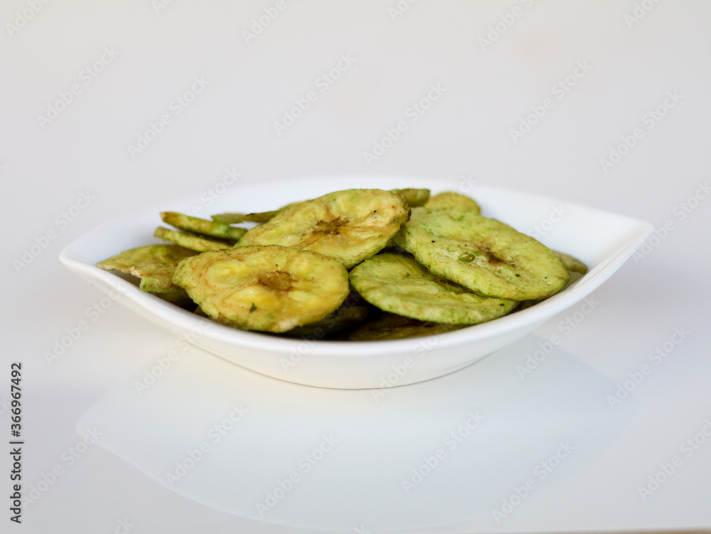 Green color banana chips with hot green chili flavor in a white bowl against white background Green color banana chips with hot green chili flavor in a white bowl against white background