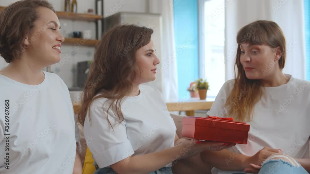 Beautiful girlfriends giving present to happy bride during party at home Beautiful girlfriends giving present to happy bride during party at home