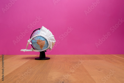 Weltkugel mit weißer Maske mit Sicht auf Nordamerika mit rosa Hintergrund auf einem Holztisch photo