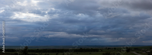 Storm clouds cover the landscape. Tragic gloomy sky. Panorama. Village in the steppe. Fantastic skies on the planet earth.