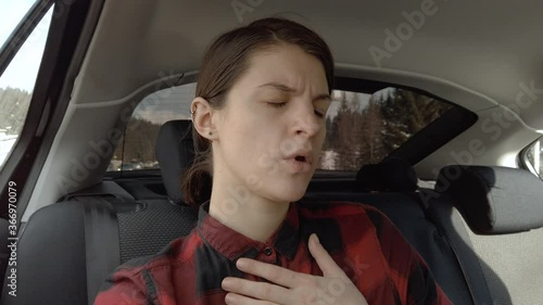Woman sits in the back seat of a car and feels bad. Female vomiting in the back seat of a car. Covers her mouth with her hand