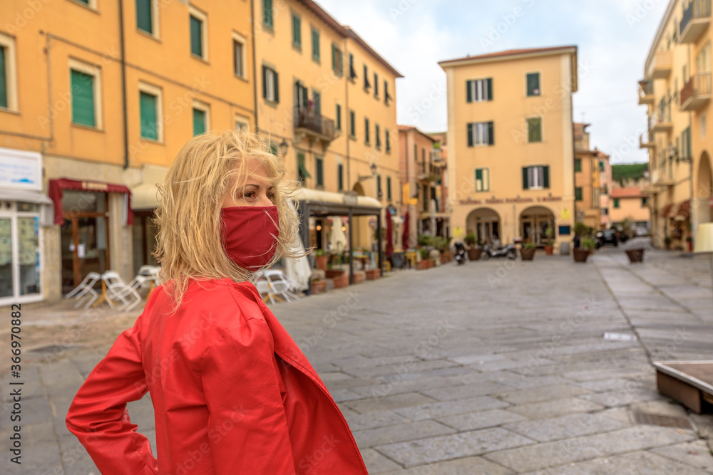 Woman with a red surgical mask during Covid-19 on Elba pier in Portoferraio downtown. Italian tourist woman travels on Elba Island. Coronavirus holiday travel in Italy, Europe, with COVID pandemic