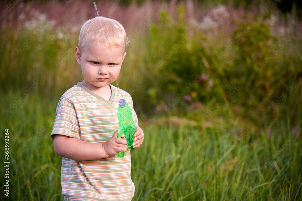 A funny two-year-old boy stands in a meadow with a water pistol. A funny two-year-old boy stands in a meadow with a water pistol.