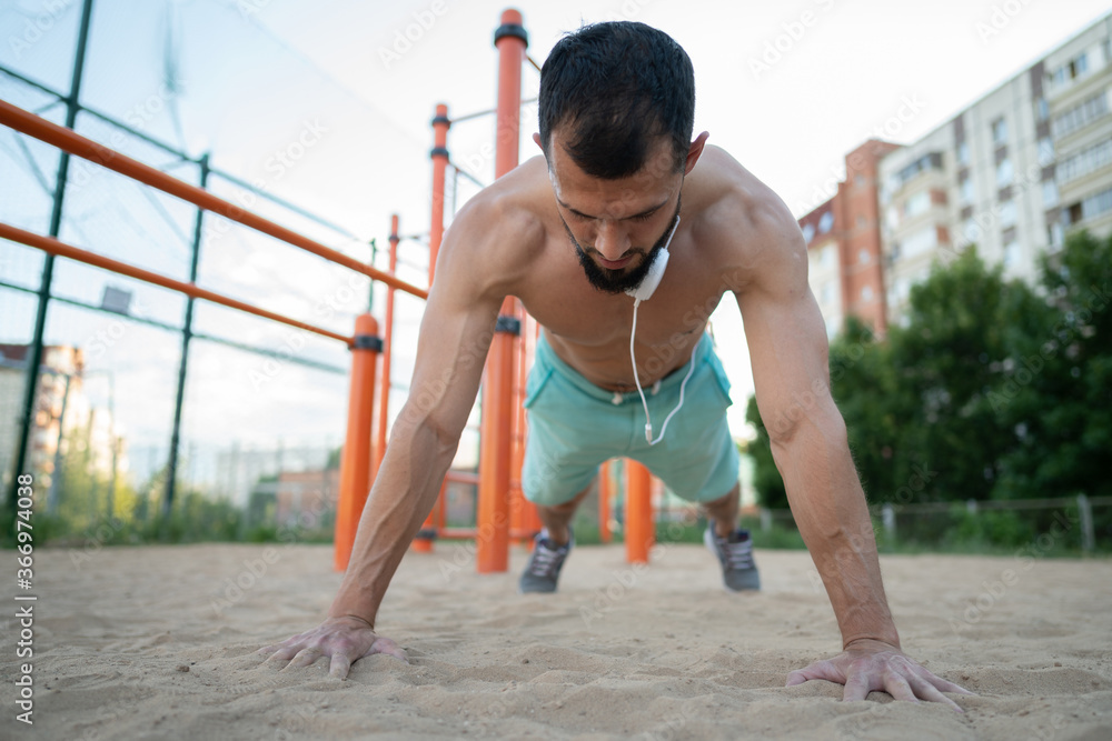 A young athlete does push-UPS on the sand in the summer. Sports, fitness, street workout concept A young athlete does push-UPS on the sand in the summer. Sports, fitness, street workout concept