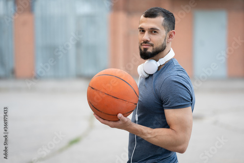 Man with headphones stands on the street with a basketball in his hands
