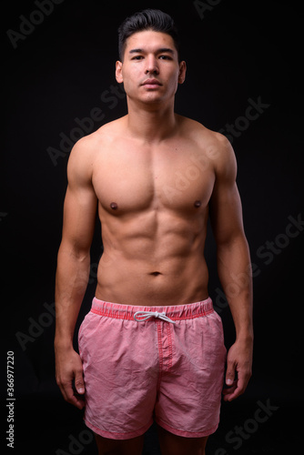Young handsome muscular man shirtless against black background