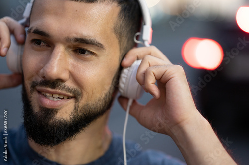 Man with headphones listens to music late at night on a city street close up