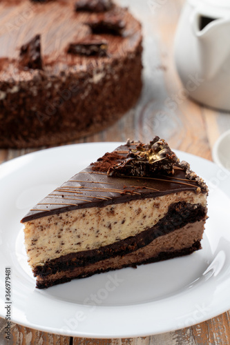 A slice of classic chocolate birthday torte on a wooden table with a cup of black tea