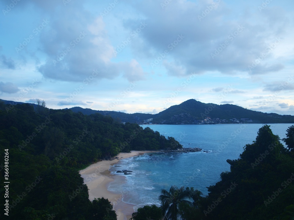 Panorama of sea bay in evening time. Green cliff covered by rainforest. Blue sea, beautiful sky with clouds. Tropical islands on the horizon. View from the top. No people, empty coast. Water, nature