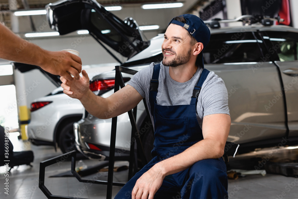 mechanic giving paper cup to cheerful coworker in cap mechanic giving paper cup to cheerful coworker in cap