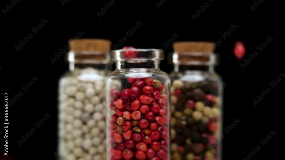 Pink peppercorns flying out of opening glass pot standing in front of pots with other spices against black background Pink peppercorns flying out of opening glass pot standing in front of pots with other spices against black background