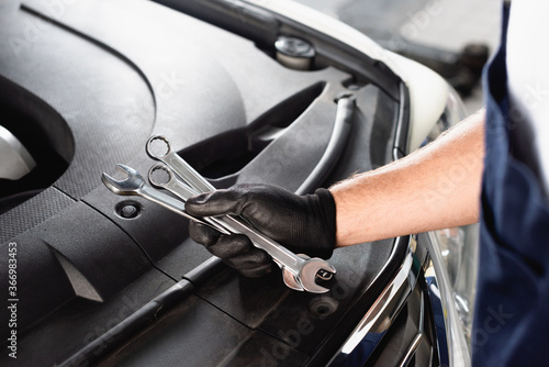 Cropped view of auto mechanic in latex glove holding wrenches near open hood