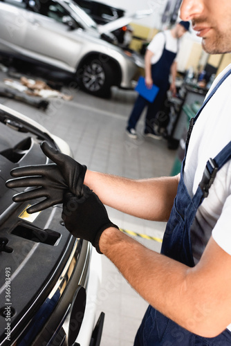 cropped view of mechanic in uniform wearing latex gloves near car in workshop
