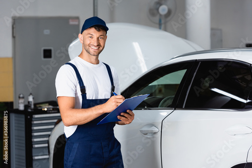 happy mechanic in cap holding clipboard near modern car © LIGHTFIELD STUDIOS