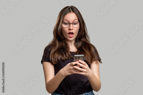 Shocked woman portrait. Overwhelming news. Stunned lady reading surprising message on phone isolated on gray. Omg really. Unbelievable information.
