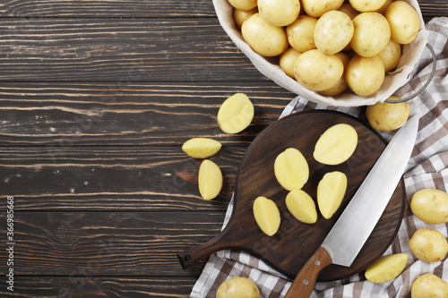 Basket full of fresh, young potatoes board, towel and knife on wooden background, top view