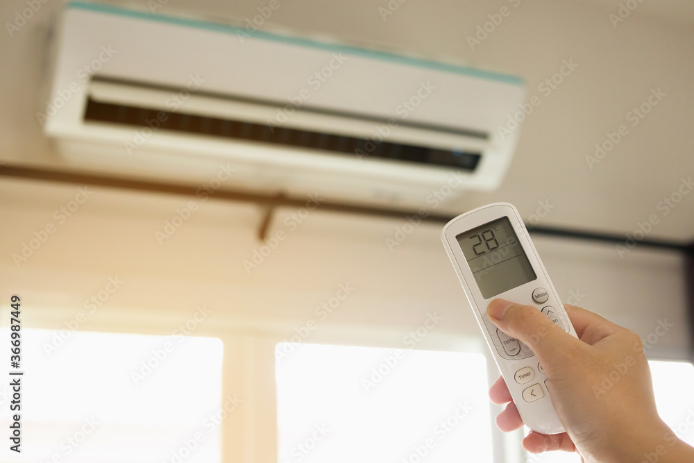 Hand with remote control directed on air conditioner inside the room Hand with remote control directed on air conditioner inside the room