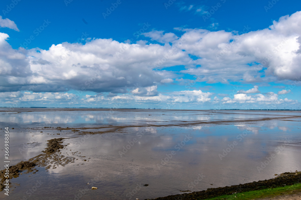 View of the Lower Saxony Wadden Sea at low tide in summer with blue sky and beautiful clouds View of the Lower Saxony Wadden Sea at low tide in summer with blue sky and beautiful clouds