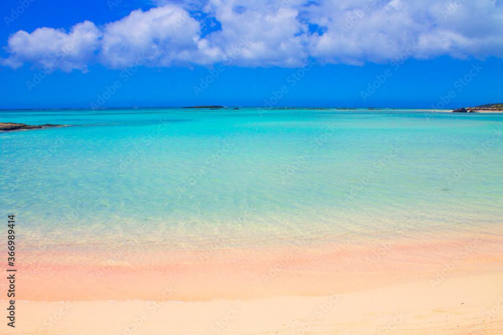 Beach with pink sand and turquoise water and clouds in blue sky.