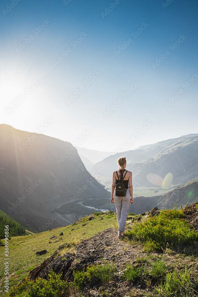 Fototapeta premium Young woman stands on the top and looks at a beautiful valley between the mountains. Backpack hiking.