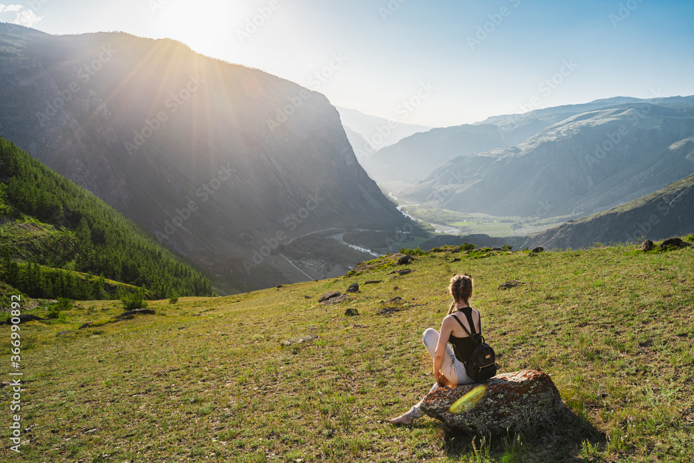 Fototapeta premium Young woman sits on the top against the background of a beautiful valley between the mountains. Backpack hiking.