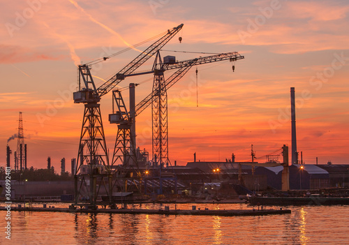 Tower cranes and elements of an oil refinery are silhouetted against a brilliant sunset near Antwerpn, Belgium.