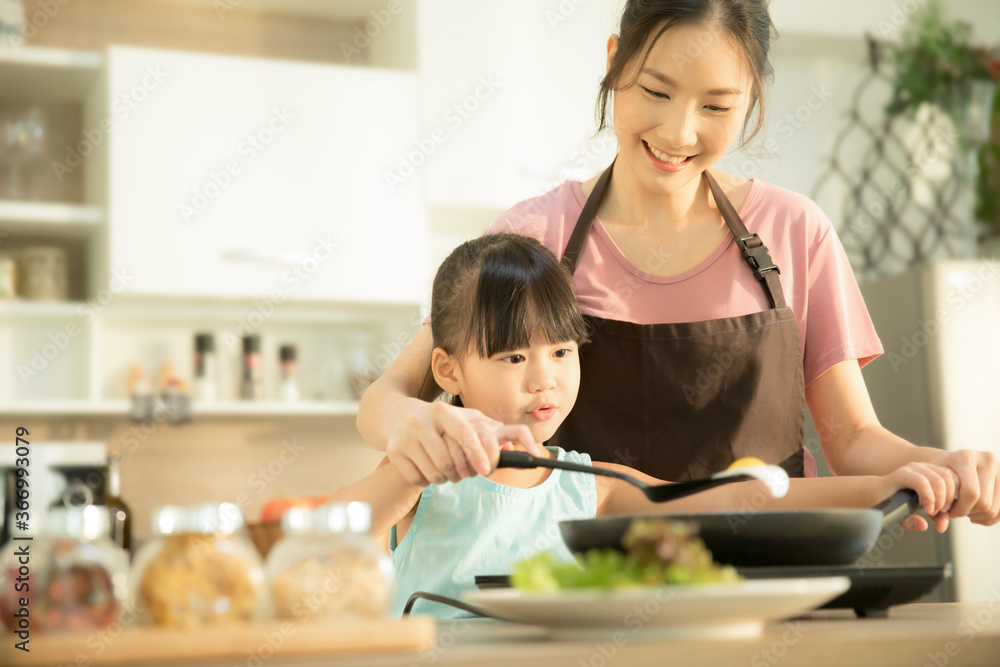 Happy Asian family in the kitchen. Mother and daughter preparing a meal with egg.