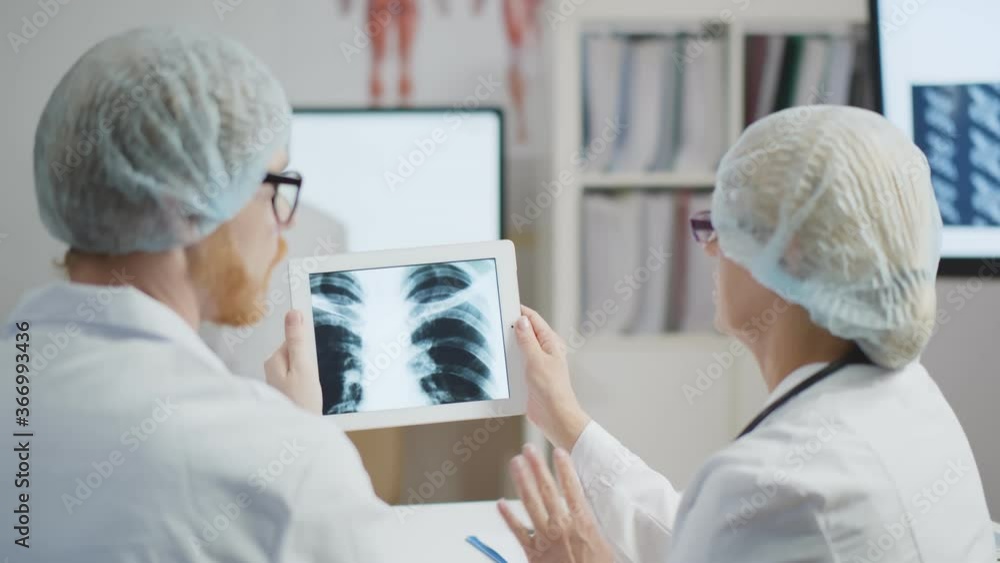 Back View of Two Doctors Having Meeting In Modern Hospital Looking At X Ray On Digital Tablet Back View of Two Doctors Having Meeting In Modern Hospital Looking At X Ray On Digital Tablet