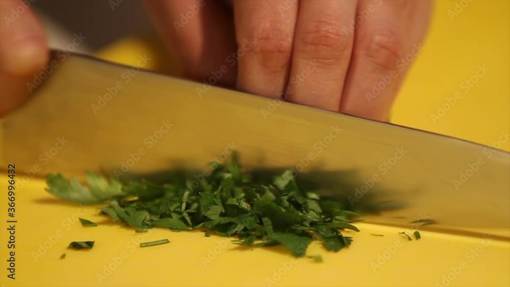 Parsley being chopped with knife on yellow board, close up Parsley being chopped with knife on yellow board, close up