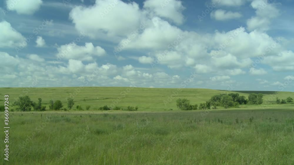Time lapse landscape with clouds passing over green prairie hills with shadows.