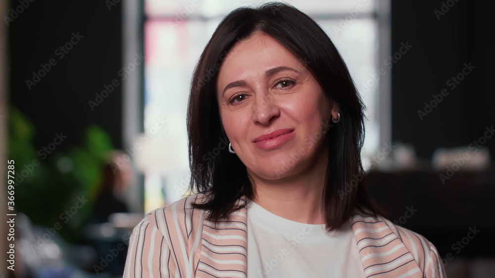 Happy attractive middle aged brunette boss business woman nods smiling at camera at modern light coworking office. Happy attractive middle aged brunette boss business woman nods smiling at camera at modern light coworking office.