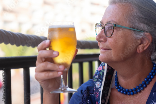 Close-up of a senior woman with floral mask due to coronavirus sitting in the restaurant enjoying a glass of fresh beer - concept of active seniors during retirement