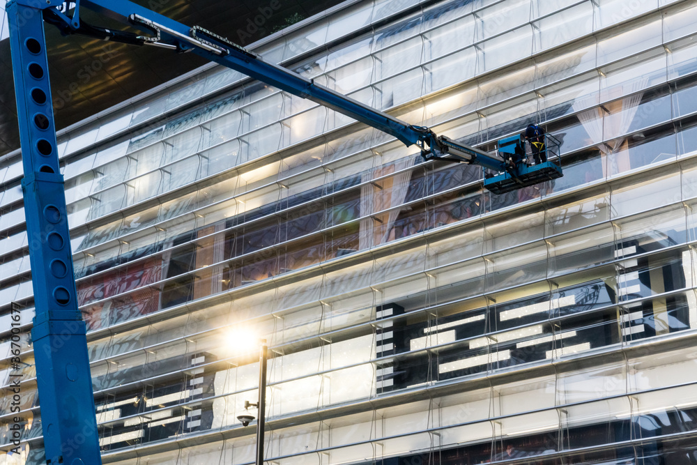 Professional windows cleaner washes windows of a building from a crane up high