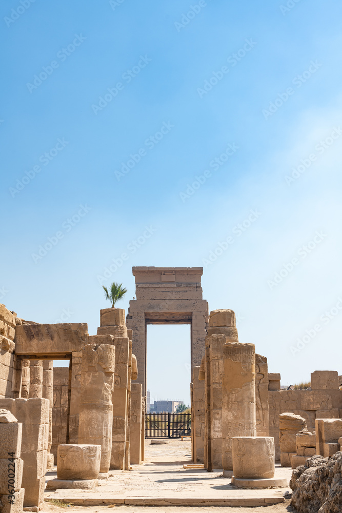 LUXOR, EGYPT - FEBRUARY 28, 2020: Gate near columns and ruins in Karnak temple with blue sky at background