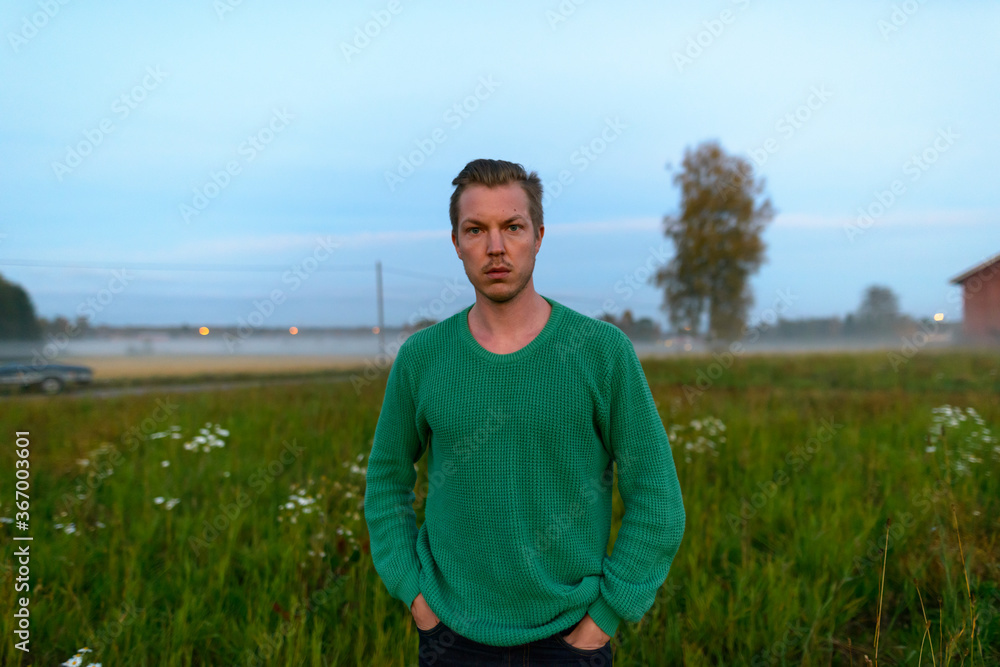 Young handsome man against grass field with fog in the break of dawn