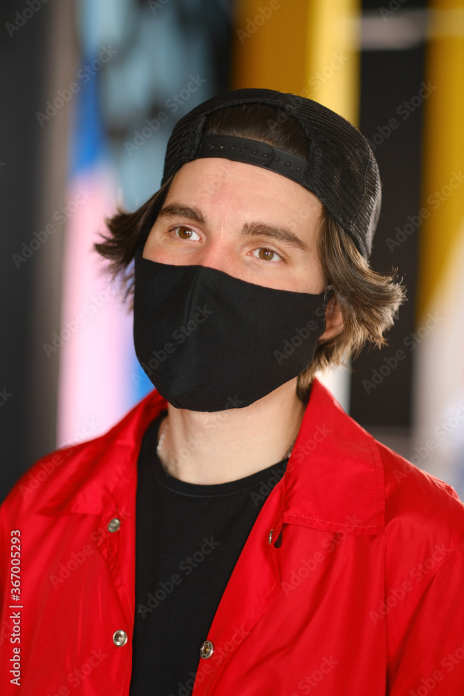 Portrait of a young man 25-30 years old in a black protective mask, black cap and red jacket. 