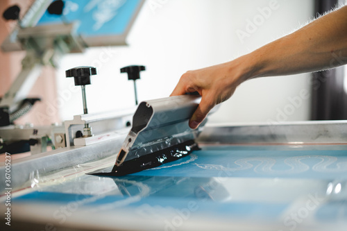 Cropped view of artisan holding squeegee with plastisol ink while working with screen printing machine in designer studio  photo
