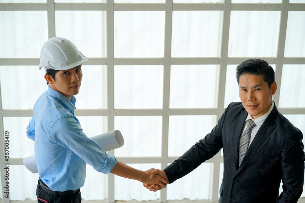 Asian engineer wearing white hard hat with blueprint meeting with business man for project