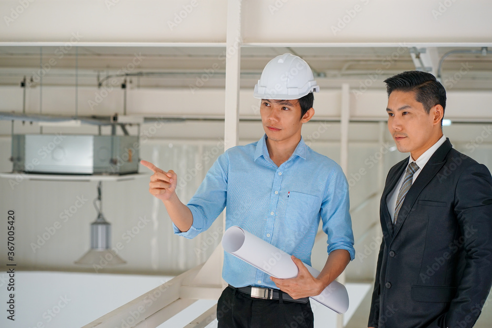 Asian engineer wearing white hard hat with blueprint meeting with business man for project Asian engineer wearing white hard hat with blueprint meeting with business man for project