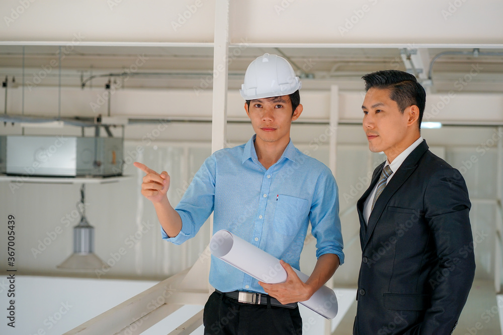 Asian engineer wearing white hard hat with blueprint meeting with business man for project Asian engineer wearing white hard hat with blueprint meeting with business man for project