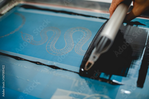 Close up of craftsman holding squeegee while applying plastisol ink on stencil on screen printing machine photo