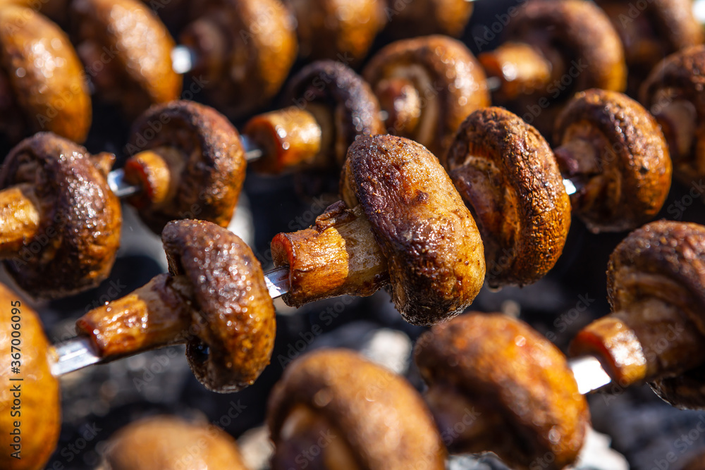 Mushrooms are roasted on fire on metal skewers over charcoal. Champignons grilled on brazier. Close-up photo made during bbq .