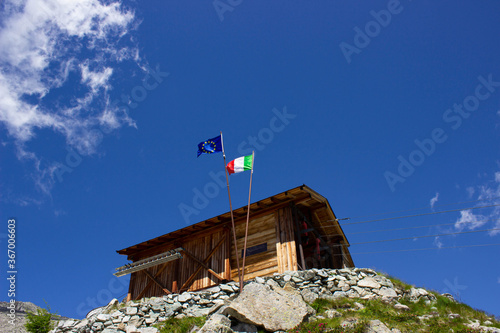 Cableway near the Mandron refuge with flags on poles against the blue sky. Italian flag and European flag near the wooden hut. photo