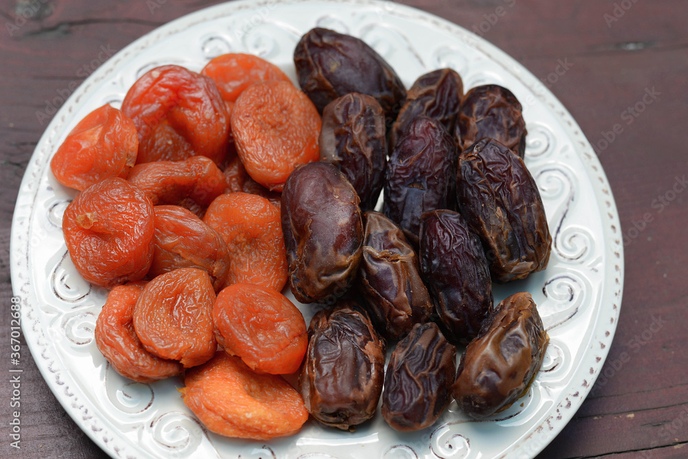 Dates and dried apricots, dried fruits on a plate on a wooden kitchen table Dates and dried apricots, dried fruits on a plate on a wooden kitchen table