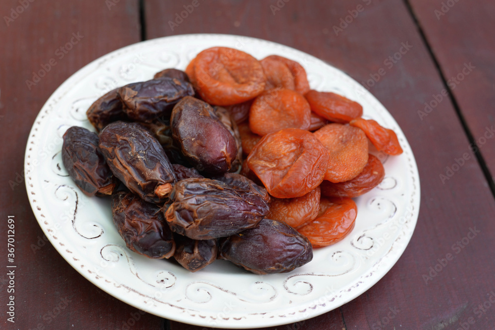 Dates and dried apricots, dried fruits on a plate on a wooden kitchen table