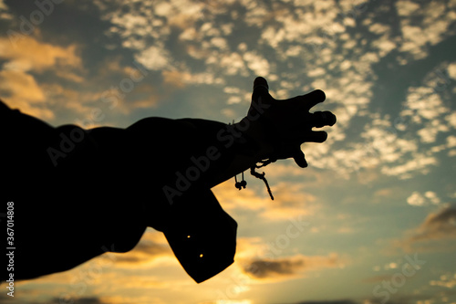 Silhouette of a hand against a sky background with clouds at sunset