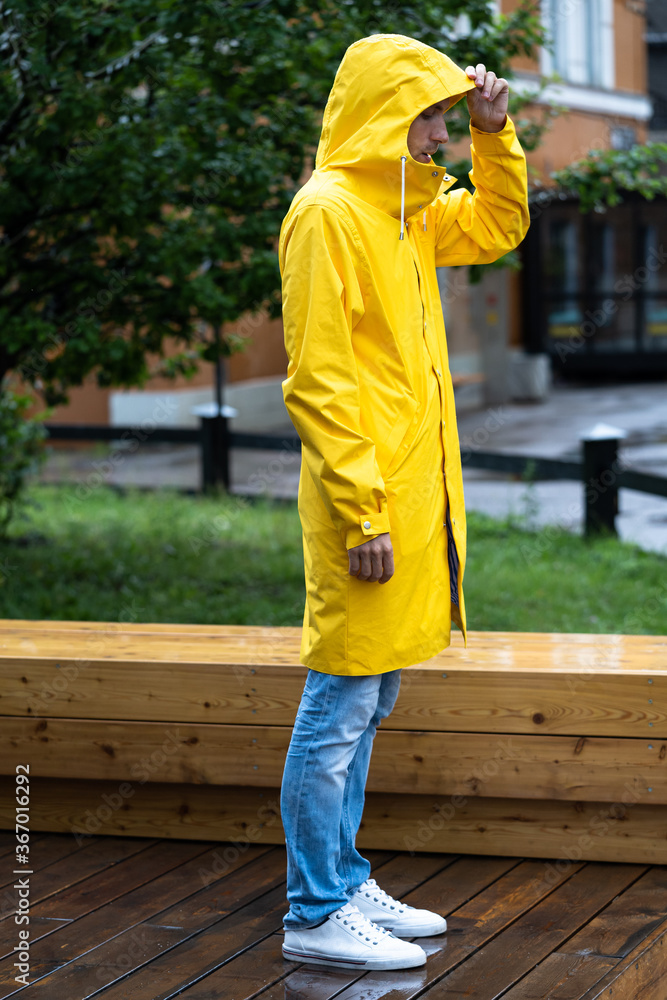Man in yellow raincoat with the hood standing on wet wooden floor in rainy weather, side view. Outdoor. Man in yellow raincoat with the hood standing on wet wooden floor in rainy weather, side view. Outdoor.