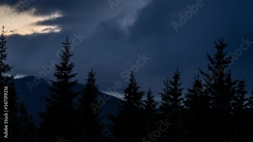 Time lapse dramatic dark thunder clouds roll over mountain valley with pine forest foreground. Epic cloudscape float over the landscape before the storm photo